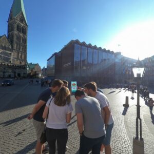 A group of young people play a city game in Bremen's Domsheide square, with St. Peter's Cathedral behind them.