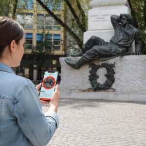 A woman playing a city game on her phone in front of the Giuseppe Garibaldi monument in Ferrara.