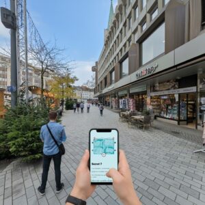 A person holds a smartphone displaying a city game map on a pedestrian street in Gelsenkirchen.