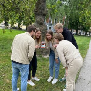 A group of five young friends stand together in a park in Norrköping, looking at a smartphone.