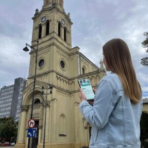 A young woman playing a city game on her phone in front of the Alexander Nevsky Cathedral in Lodz.