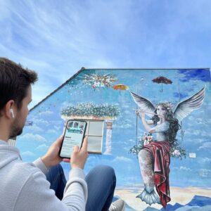 A man views a City Game on his phone before a large mural of a winged siren in Almere.