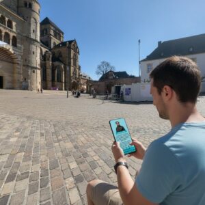 A man plays a city game on his phone in the square in front of the Trier Cathedral.
