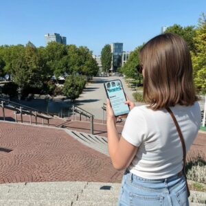 A woman stands on brick and stone steps in Cologne, playing a city exploration game on her smartphone.