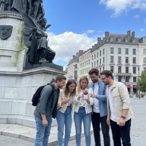 Five young adults stand by the Daniel O'Connell Monument in Dublin, smiling and looking at a smartphone.