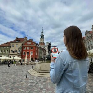 A woman stands in Poznań's Old Market Square playing a city game on her smartphone.