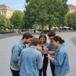 A group of five friends in denim jackets huddle around a smartphone in a city square in The Hague.