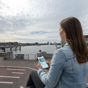 A young woman in a denim jacket plays a city game on her phone by the Zaan river in Zaandam.