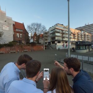 Four young adults gathered around a smartphone while playing an outdoor city game in Bremen's Schlachte district.