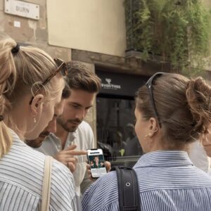 A group of young friends gathered together on a street in Karlskrona, looking at a smartphone.