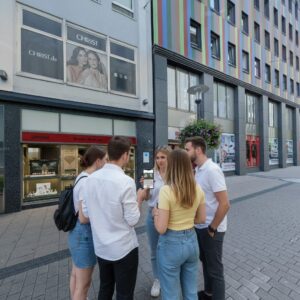 A group of five young friends stand together on the Kettwiger Straße in Essen looking at a smartphone.