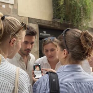 A group of young friends stand together on a street in Dresden, looking intently at a smartphone.