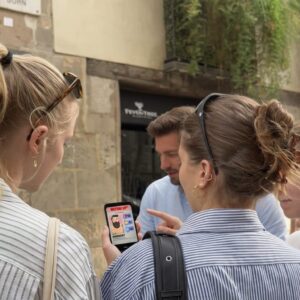 A group of young friends stand on a street in Terneuzen, looking at a game on a smartphone.