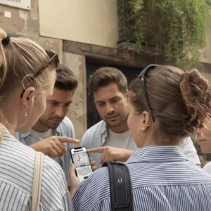 A group of young friends huddle together on a street in Orebro, looking at a map on a smartphone.
