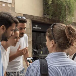 A group of young friends huddle together on a city street in The Hague, looking at a smartphone.