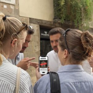 A group of friends stand together on a street in Corfu, looking at a Sherlock game on a smartphone.
