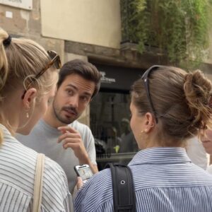 A man points to a smartphone screen while talking to three young women on a street in Zagreb.