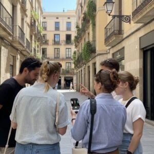 A group of five young people stand together in a narrow stone street in San Marino, looking at a smartphone.