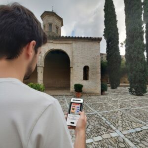 A man plays a Sherlock-themed city game on his phone in a cobblestone courtyard at the Alcázar of Jerez.