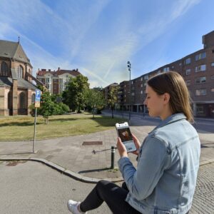 A woman playing a game on her phone in a park next to St. Peter's Church in Malmö.