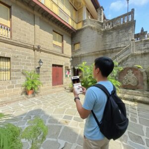 A young man with a backpack uses his smartphone in the historic stone courtyard of Casa Manila in Manila.