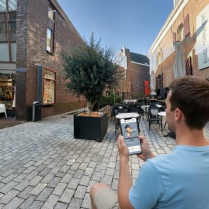 A man sits on a cobblestone courtyard in Nijmegen while playing a city game on his smartphone.