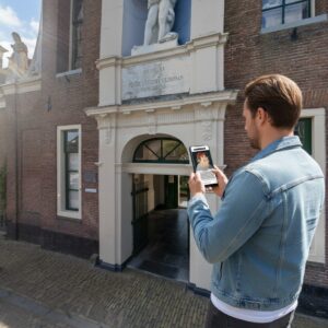 A man in a denim jacket plays a city game on his phone before the historic Provenhuis van Wildeman in Alkmaar.