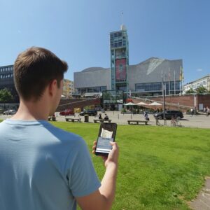 A young man plays a city game on his phone in the park in front of the Rosengarten congress center in Mannheim.