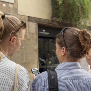 Three young women seen from behind look at a smartphone while exploring the streets of Nordlingen.
