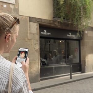 A woman with a blonde braid looks at a city game on her phone on a historic cobblestone street in Oslo.