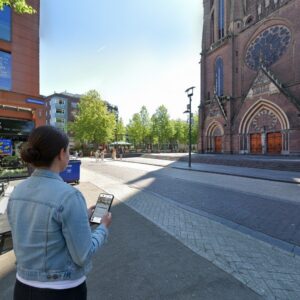 A woman plays a city game on her phone in front of the historic Catharinakerk church in Eindhoven.