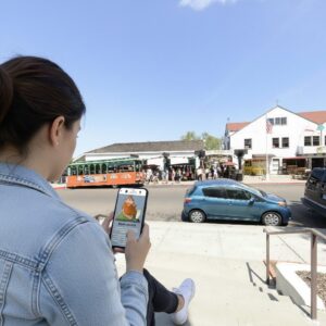A woman sits on steps in Old Town San Diego, playing a city exploration game on her smartphone.