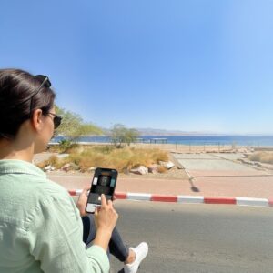 A woman sits by the Red Sea in Eilat, playing a game on her smartphone.