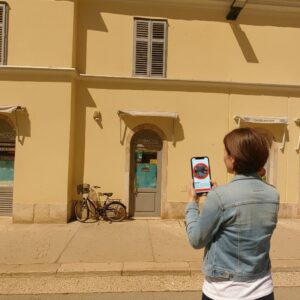 A woman in a denim jacket stands on a street in Rovinj, playing a City Game on her smartphone.