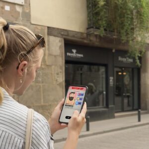 A young woman with blonde braided hair looks at a mobile game on her phone on a street in Namur.
