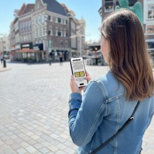 A woman seen from behind plays a City Game on her smartphone on the Grote Markt in Zwolle.