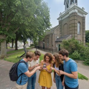 Five friends play a city game on a smartphone in front of the Kerkje aan de Zee church in Urk.