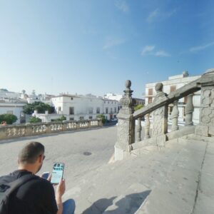 A man sits on the historic stone steps of the Jerez de la Frontera Cathedral, looking at his phone.