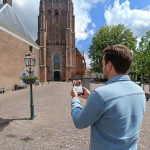 A man plays a city game on his phone in the square in front of the Grote Kerk in Wijk bij Duurstede.