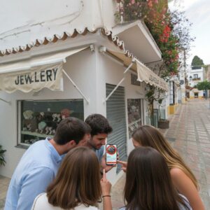 A group of friends look at a smartphone while playing a city exploration game in Marbella.