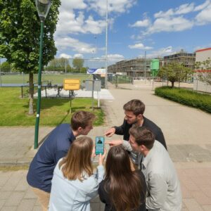 A group of five young adults gather around a smartphone during an outdoor city game in Montfoort.