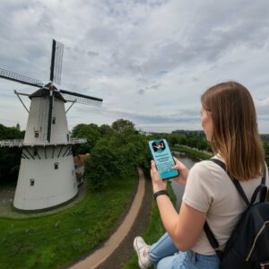 A woman looking at a smartphone with the historic De Hoop windmill in the background in Middelburg.