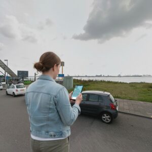 A woman stands by the water in Hoek van Holland, looking at a city game on her phone.