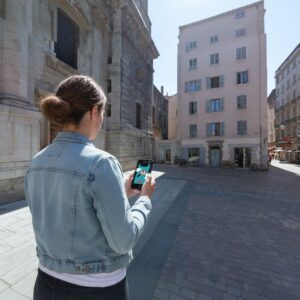 A woman stands in a sunny square in Toulon, using her smartphone to play a city exploration game.
